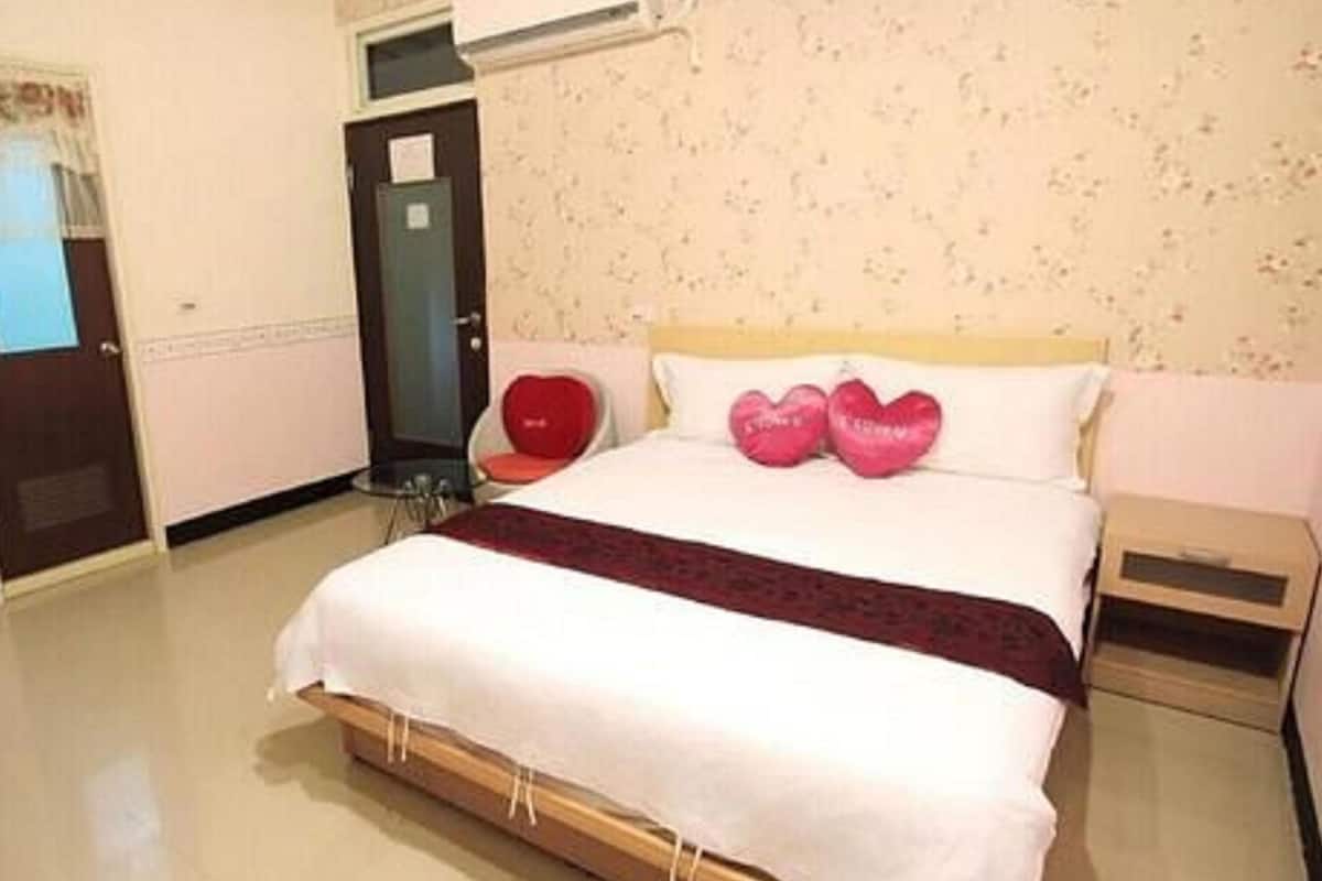 A hotel room with a large bed, a bedside table, a chair, and a door.