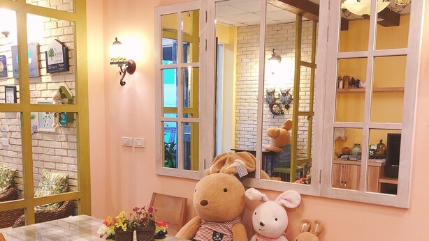 Un comedor con una mesa de vidrio, sillas de madera y un gran oso de peluche.