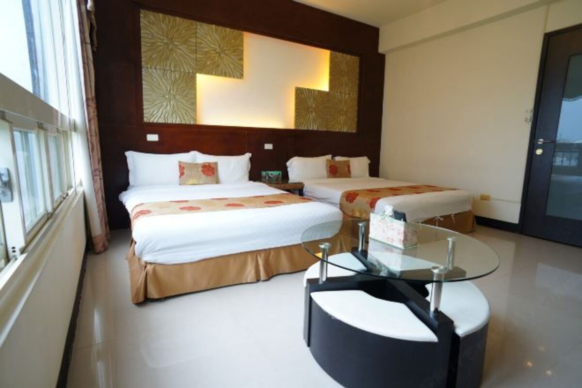 A hotel room with two beds, a glass coffee table, and a decorative wall panel.
