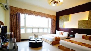 Una habitación de hotel con dos camas, una mesa redonda y un amplio ventanal con cortinas.