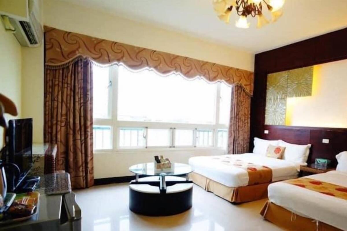 A hotel room with two beds, a round table, and a large window with curtains.
