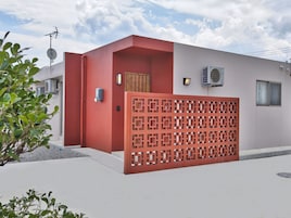 Un edificio moderno con fachada roja y blanca, una entrada con portón y una unidad de aire acondicionado en la pared exterior.
