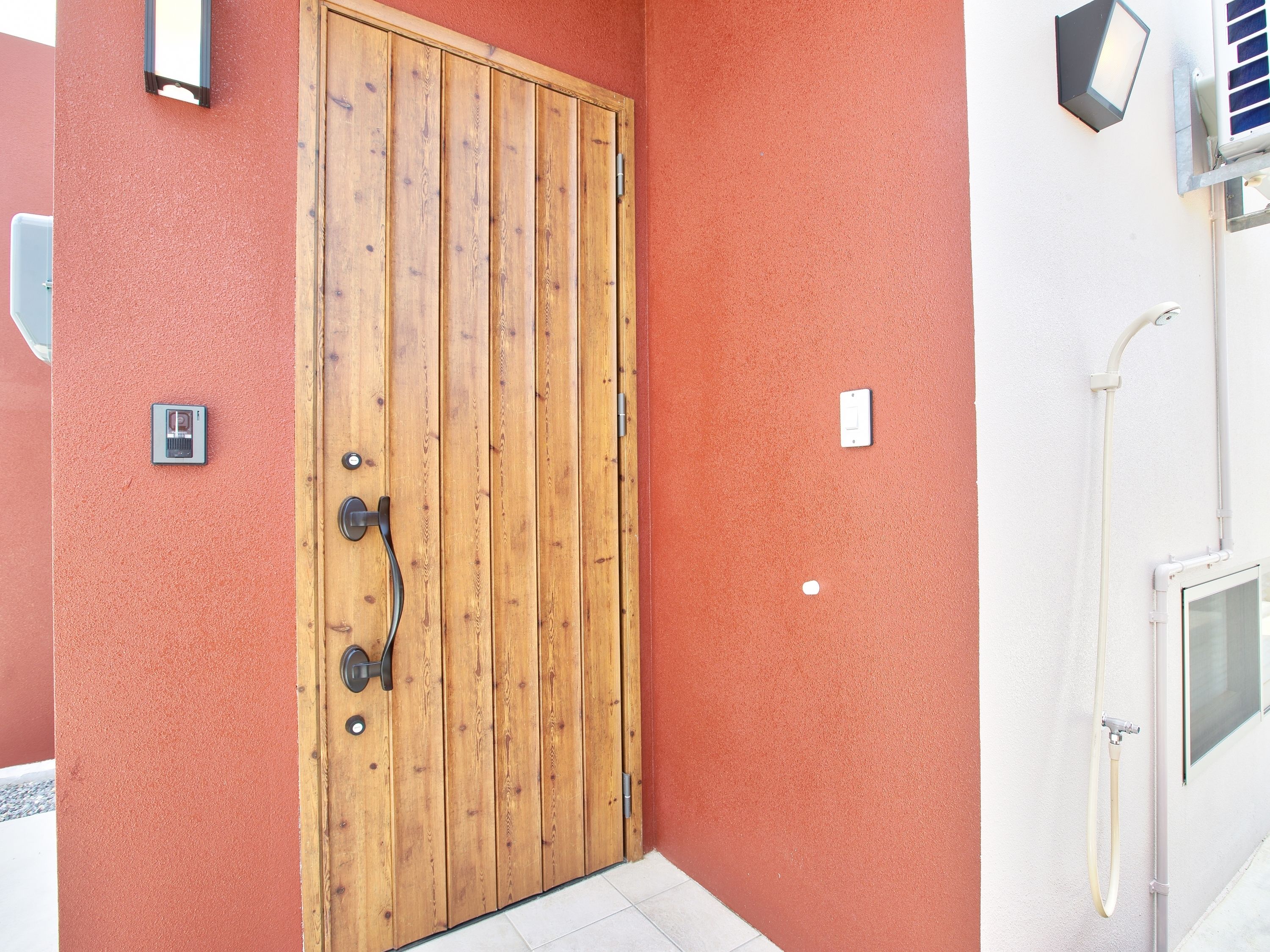 A wooden door with a handle, a wall-mounted light, and a window with a view of the sky.