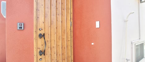 Una puerta de madera con manija, una luz empotrada en la pared y una ventana con vista al cielo.