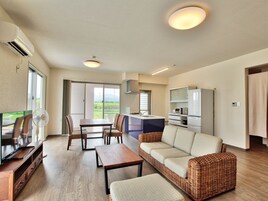 Una sala de estar moderna con un sofá, una mesa de comedor y un televisor. Hay una cocina con refrigerador y microondas.