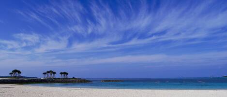 A beach with white sand, calm blue waters, and a clear sky.
