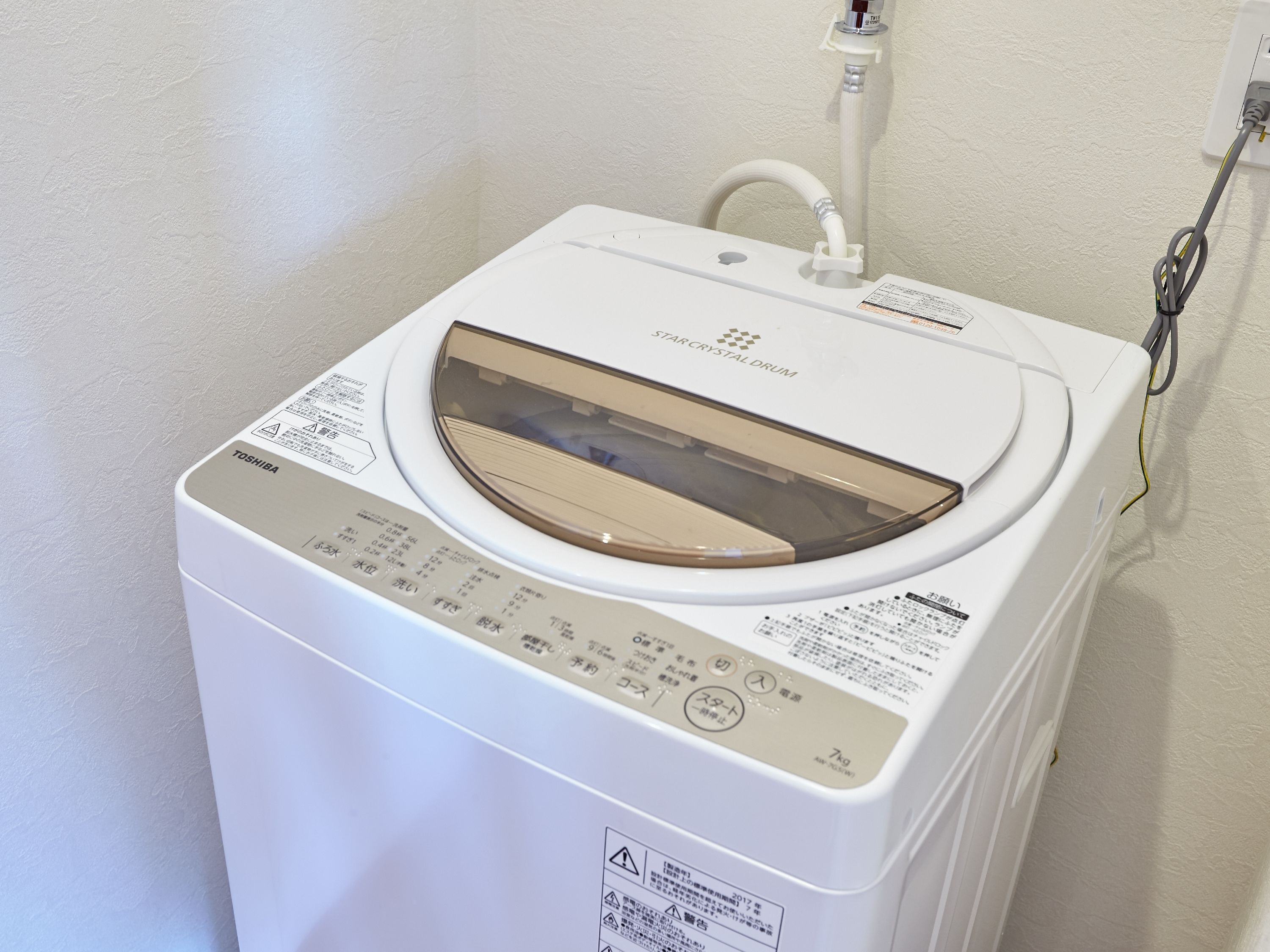 Eine weiße Waschmaschine mit Bedienfeld und transparenter Tür, angeschlossen an eine Steckdose.