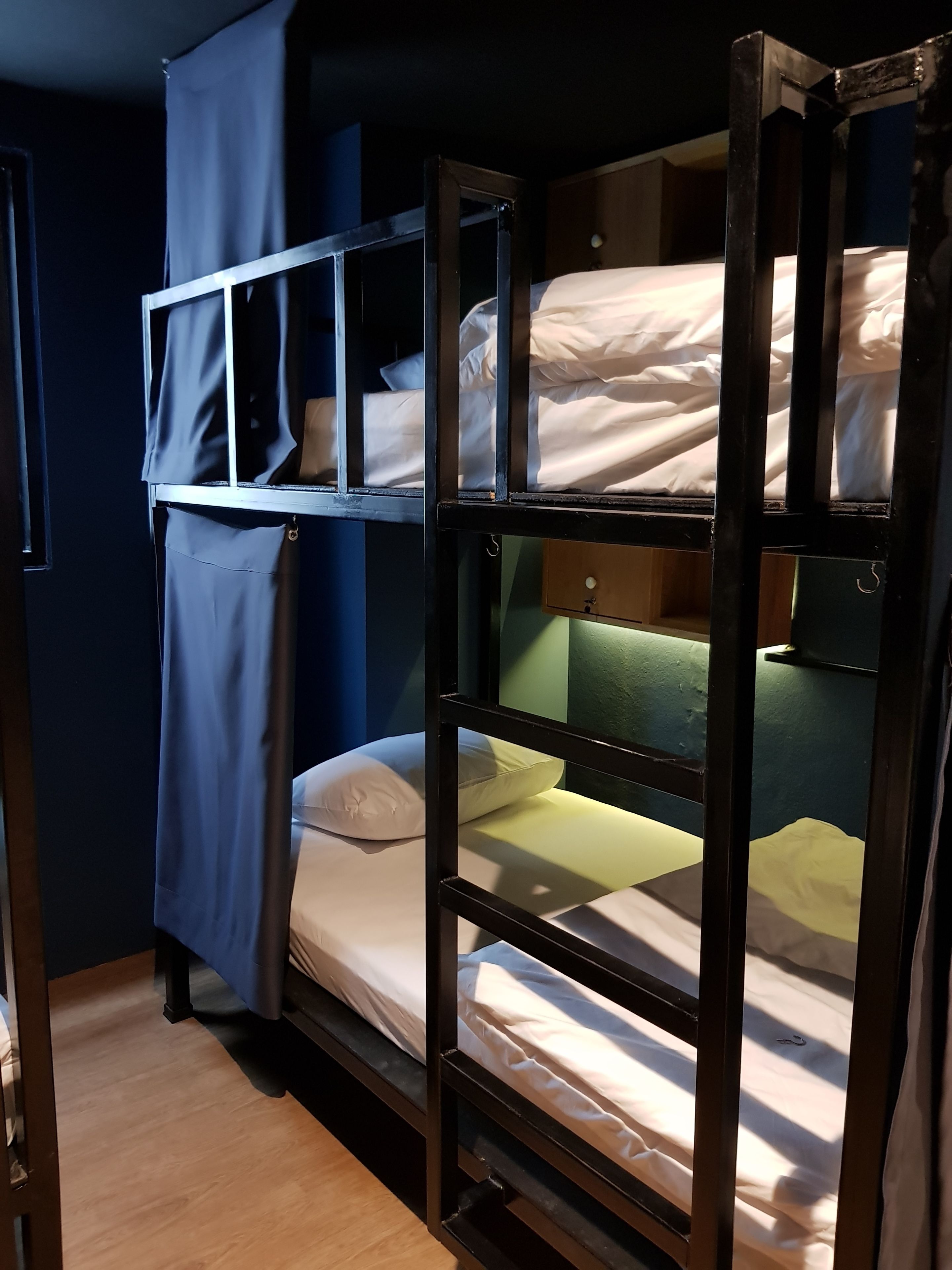 Un lit superposé avec un rideau bleu, un plancher en bois et un mur vert.