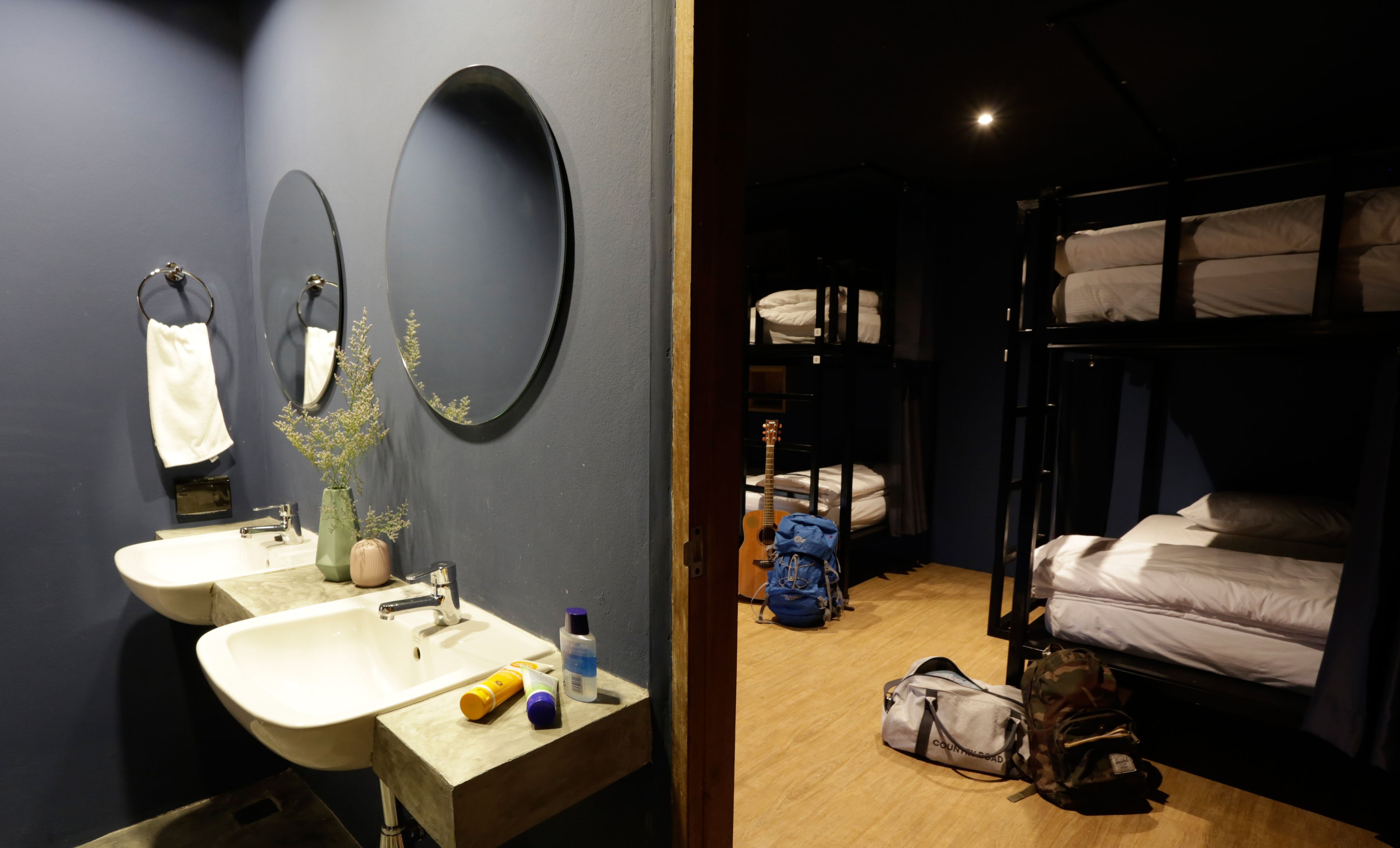 A room with a sink, two mirrors, a vase with flowers, and a bunk bed with pillows.