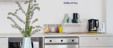 A kitchen with a sign that reads "All day Coffee & Tea", a coffee maker, a toaster, and jars on the counter.