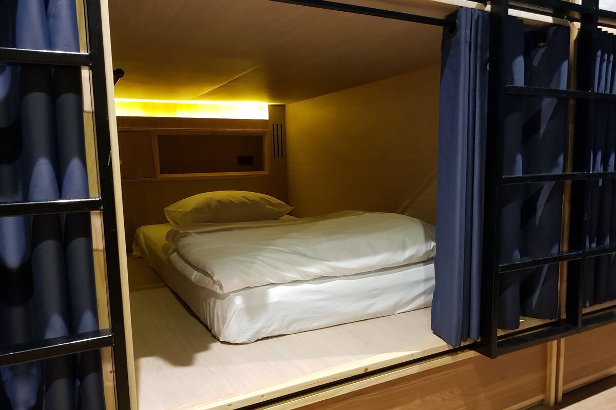 Una habitación pequeña con cama, mesita de noche y lámpara de pared.