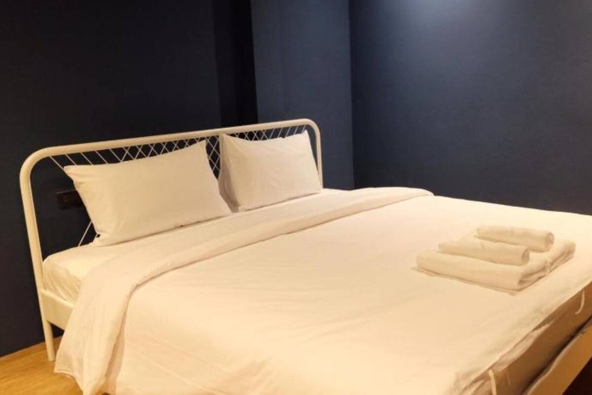 Una cama bien hecha con sábanas y almohadas blancas, suelo de madera y paredes oscuras.