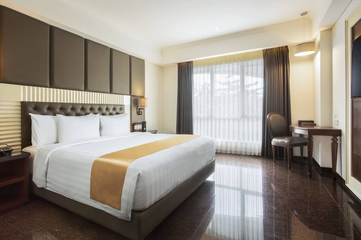 A hotel room with a large bed, a desk, a chair, and a window with curtains.