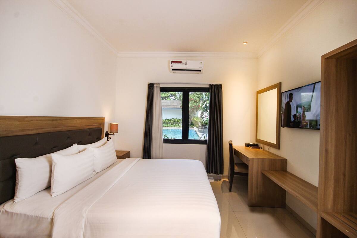 A hotel room with a large bed, a desk, a television, and a window with a view of a swimming pool.
