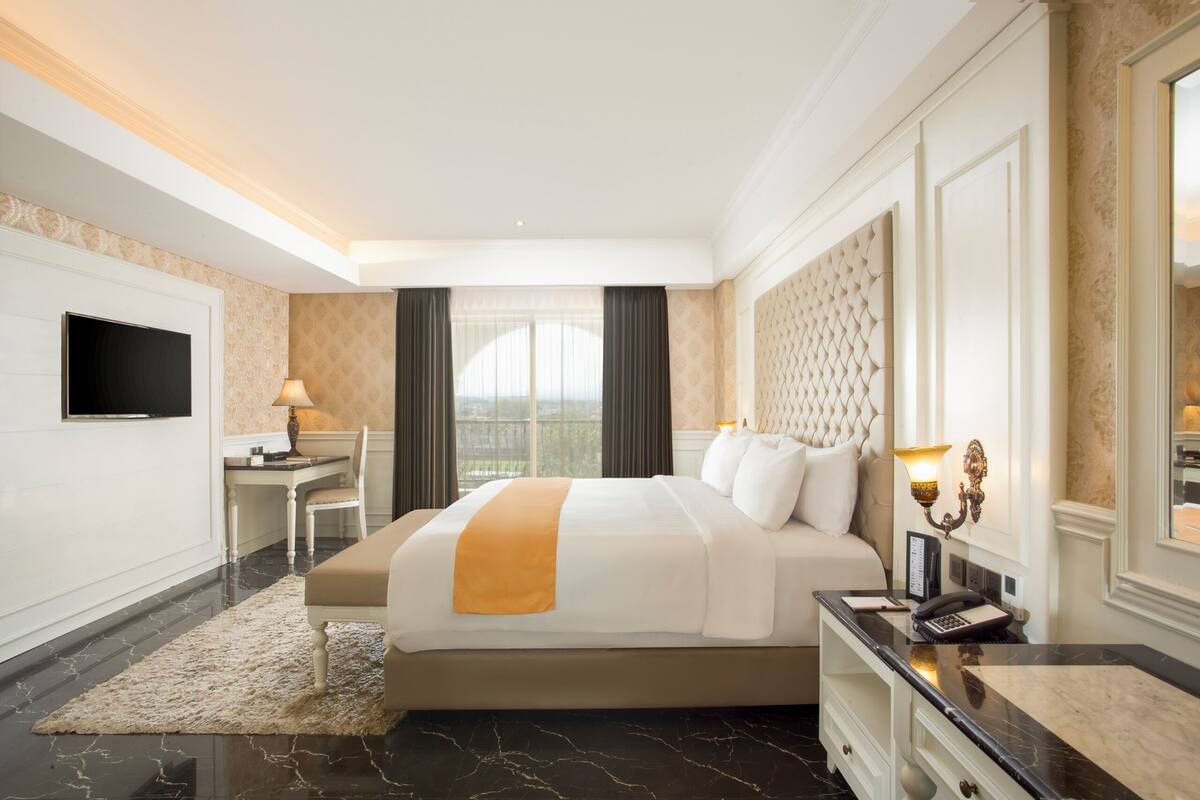 A hotel room with a large bed, a desk, a flat-screen TV, and a view of the city.