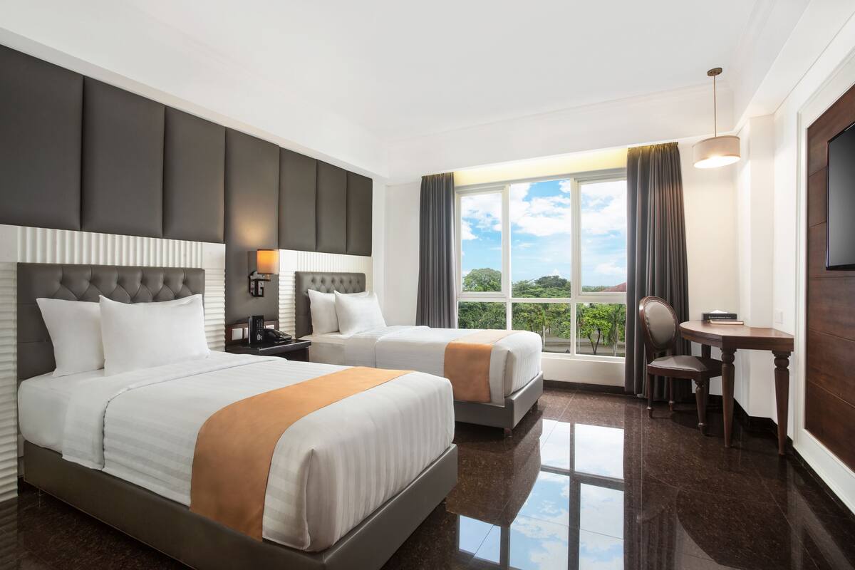 A hotel room with two beds, a desk, and a chair.
