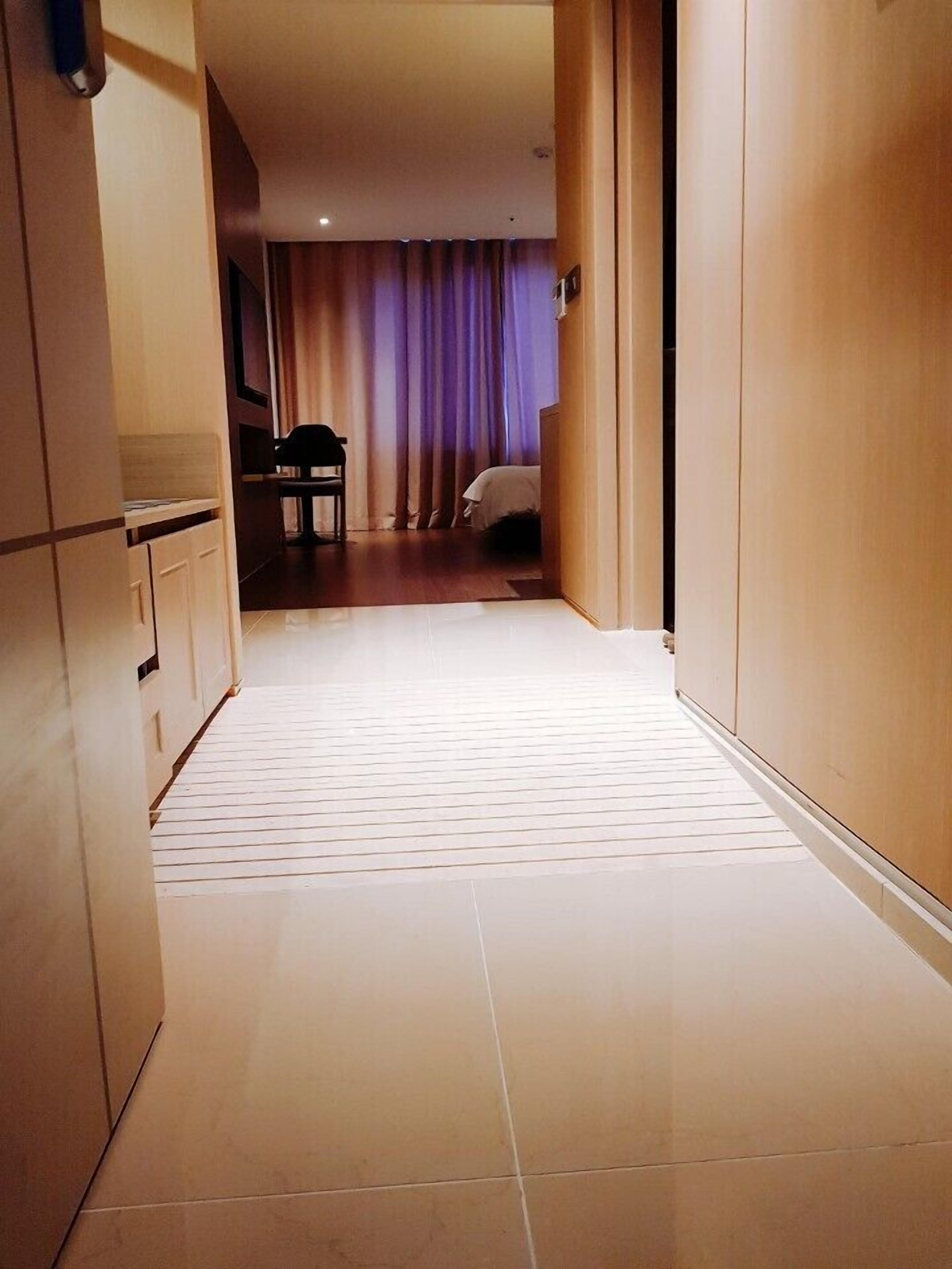 A narrow hallway with a tiled floor leading to a room with a bed and a chair.