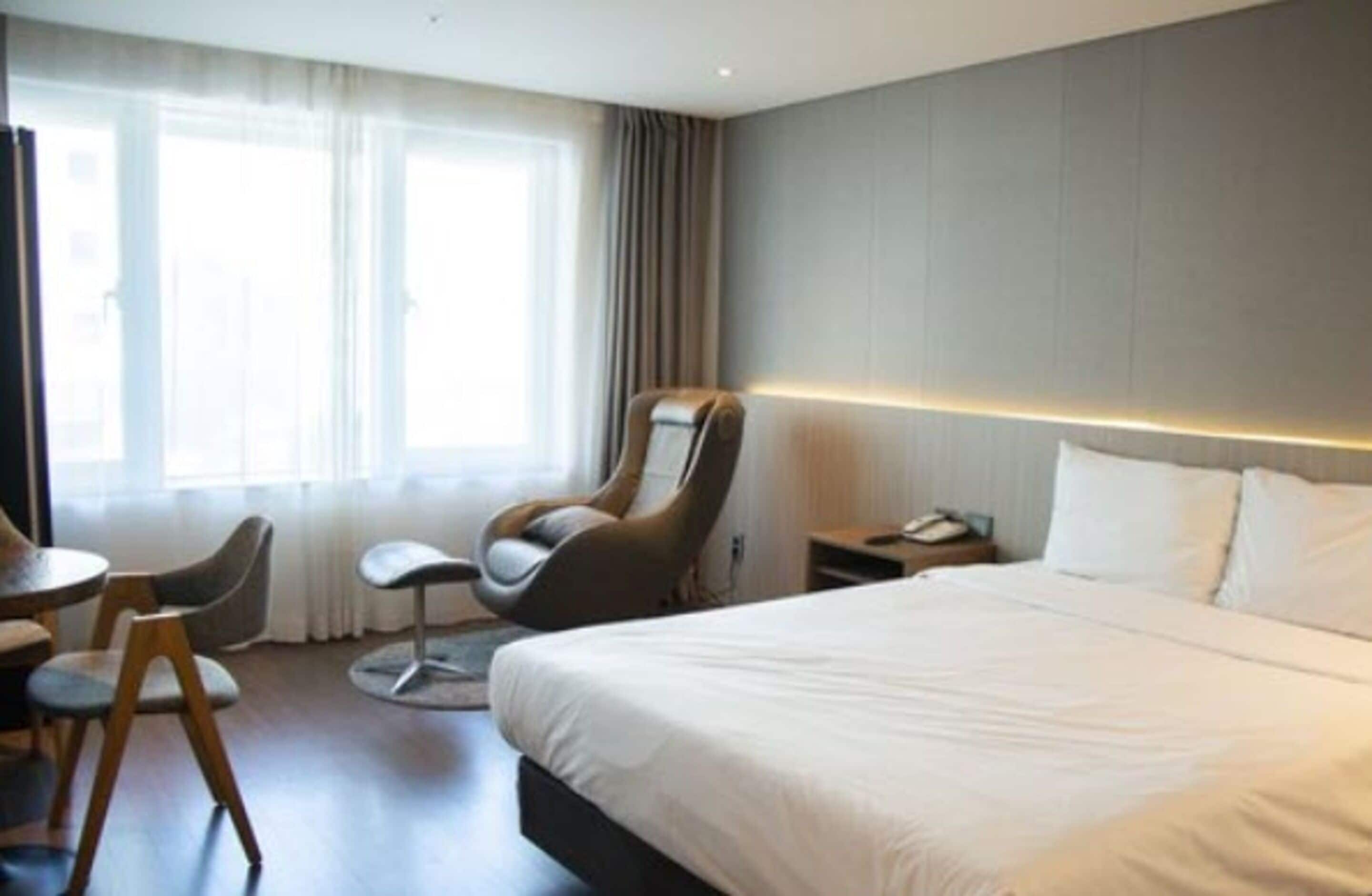 Una habitación de hotel con una cama grande, una silla, un escritorio y un ventanal con cortinas.