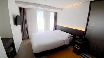 A hotel room with a bed, a television, a nightstand, and a window with curtains.
