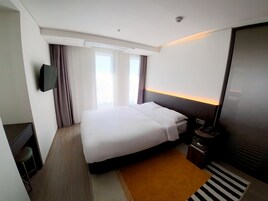 A hotel room with a bed, a television, a nightstand, and a window with curtains.