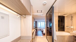 A modern hotel room with a wooden floor, a large bed, a desk, and a bathroom with a bathtub and shower. - The First70 Hotel (Seogwipo)