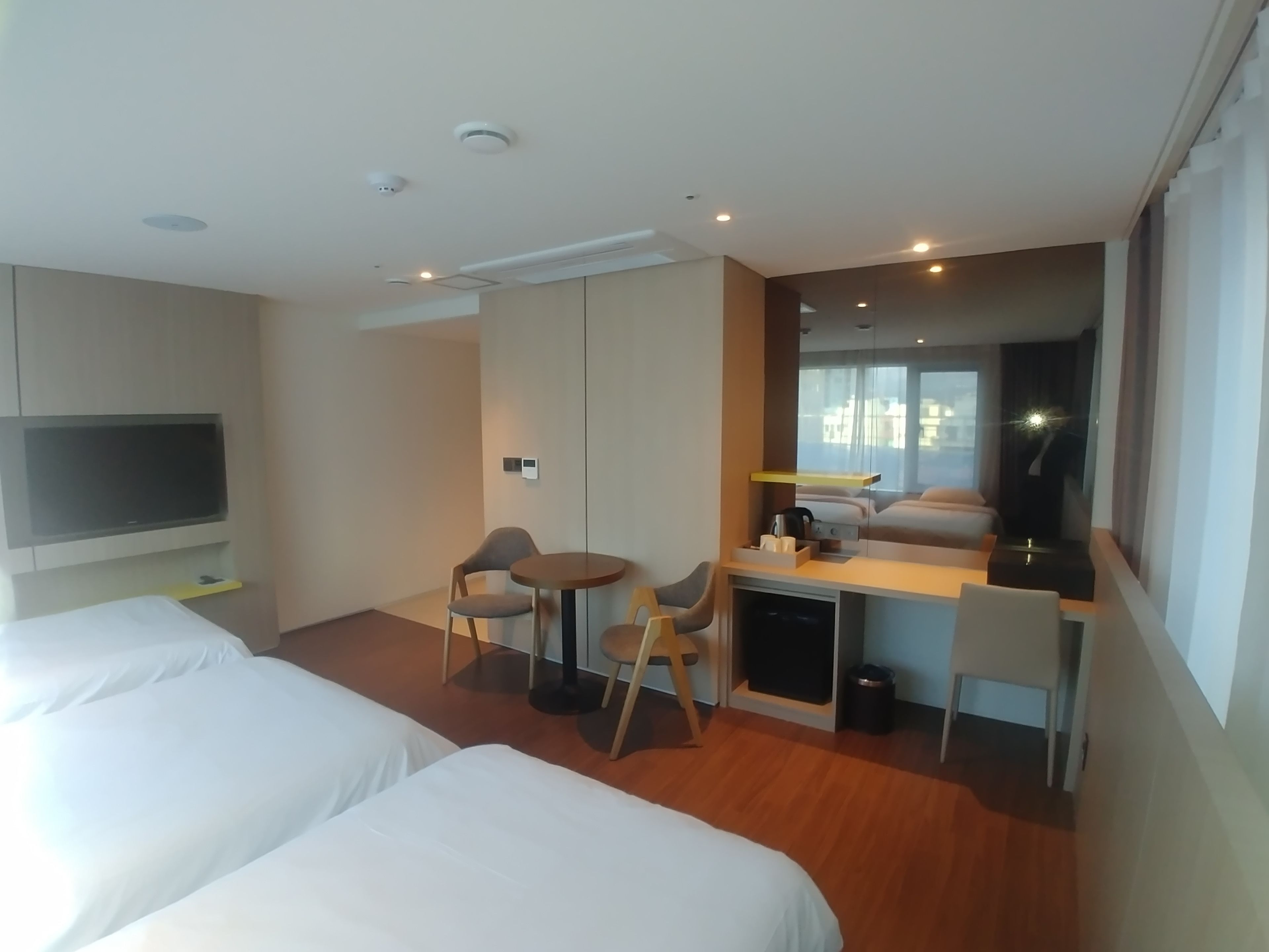 A hotel room with two beds, a desk, a chair, a TV, and a window with a view of buildings.