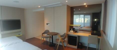 A hotel room with two beds, a desk, a chair, a TV, and a window with a view of buildings.