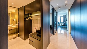 A modern hotel room with a built-in wardrobe, a small seating area, and a view of the hallway. - The First70 Hotel (Seogwipo)