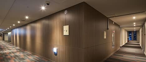 A hotel corridor with wooden panel walls, a patterned carpet, and recessed lighting.