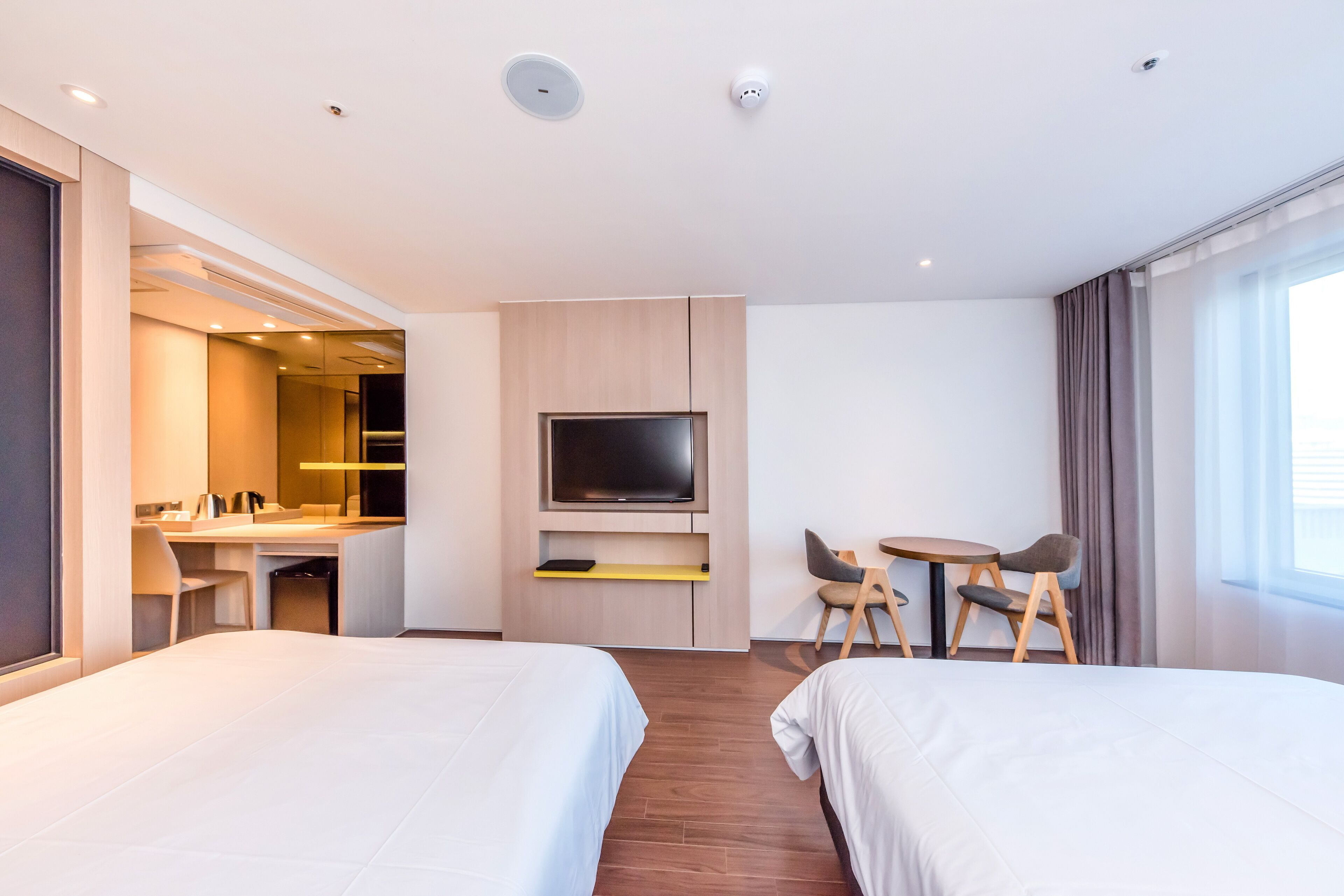 A hotel room with two beds, a TV, a desk with a chair, and a small table with chairs.