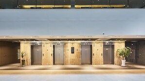 A modern hotel lobby with a central elevator, potted plants, and a clean, well-lit interior. - The First70 Hotel (Seogwipo)