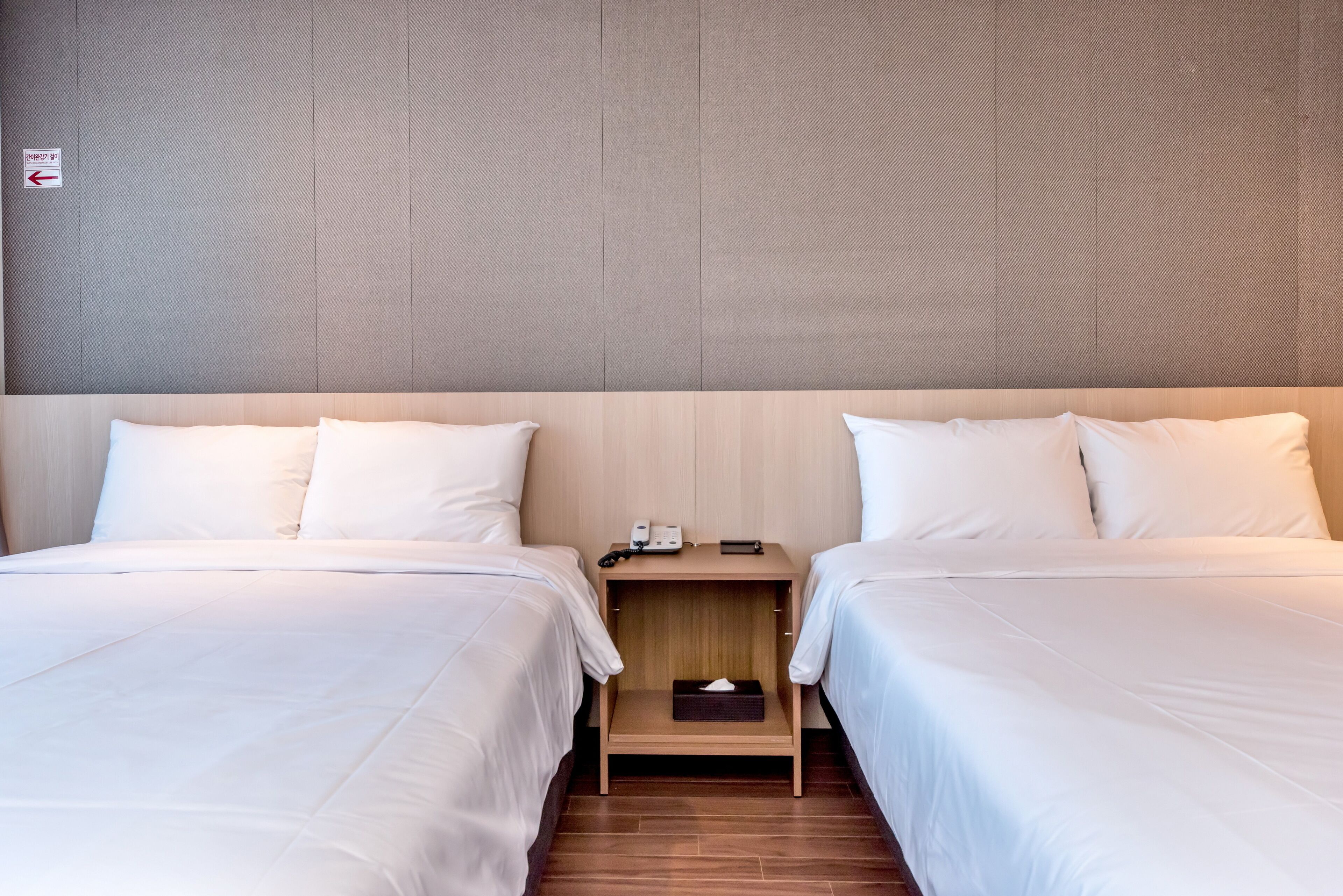 Une chambre d’hôtel avec deux lits, une table de chevet en bois placée entre eux, et un mur sobre.