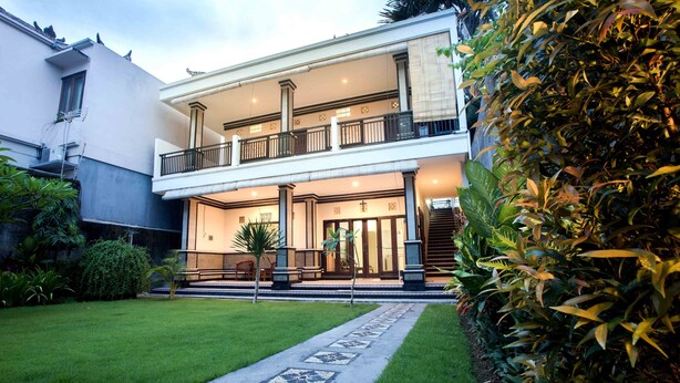 A two-story building with a balcony, a well-maintained lawn, and a pathway leading to the entrance.
