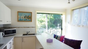 A kitchen with a microwave, sink, and cabinets. There is a painting on the wall and a window with a view of greenery. - Moon House (Diamond Creek)