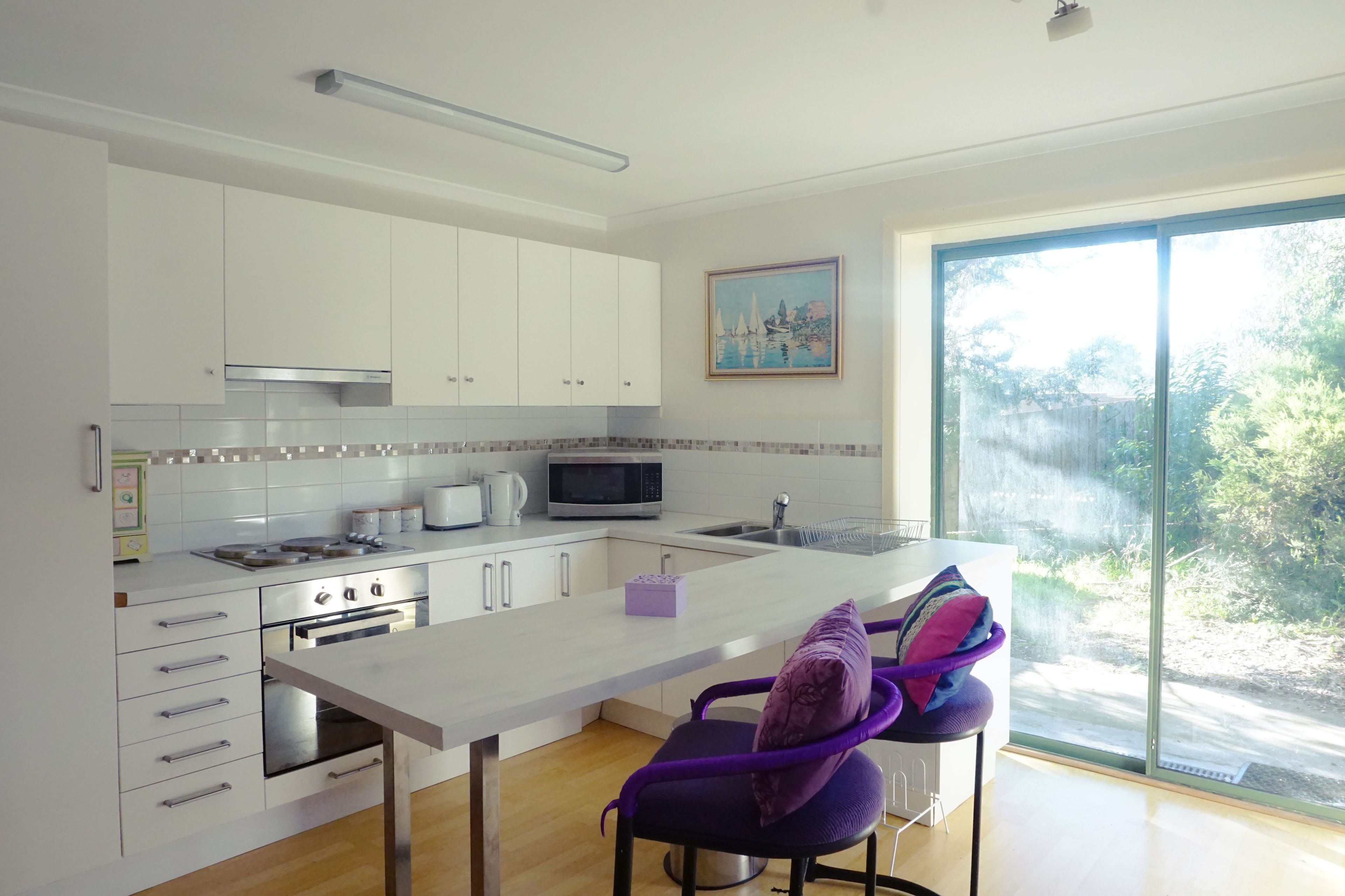 A modern kitchen with white cabinets, a microwave, and a large window offering a view of greenery.