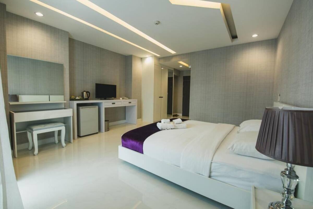 A modern hotel room with a bed, desk, chair, TV, and a mirror.