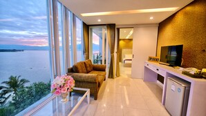 A modern hotel room with a large window offering a view of the sea, a cozy seating area with a vase of flowers, and a small kitchenette. - Phuglong Hotel (Phayao)