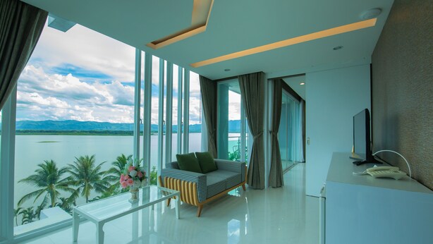 A modern room with a large window, a sofa, a small table, and a desk with a phone. - Phuglong Hotel (Phayao)