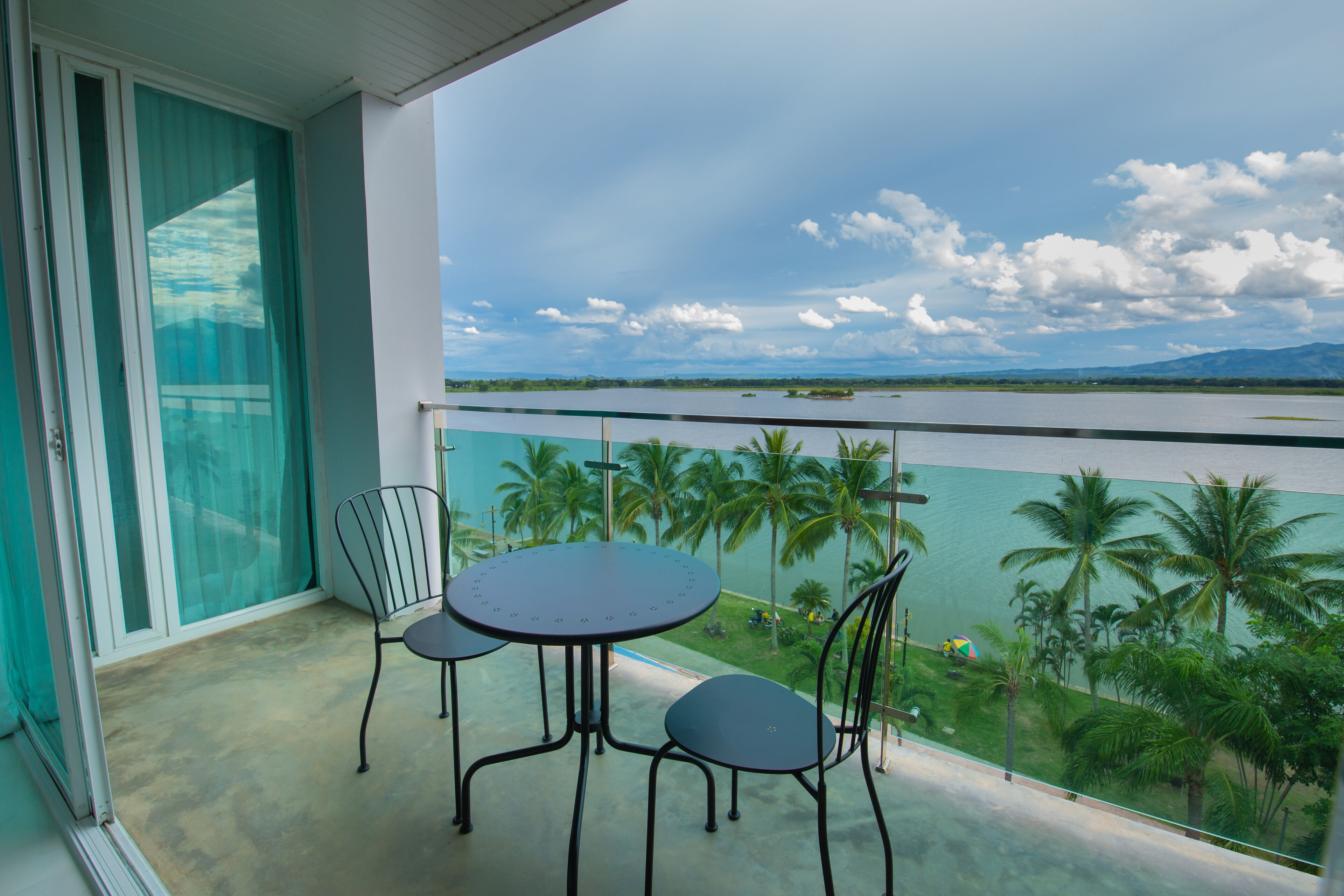 A balcony with a table and chairs, overlooking a body of water and palm trees.