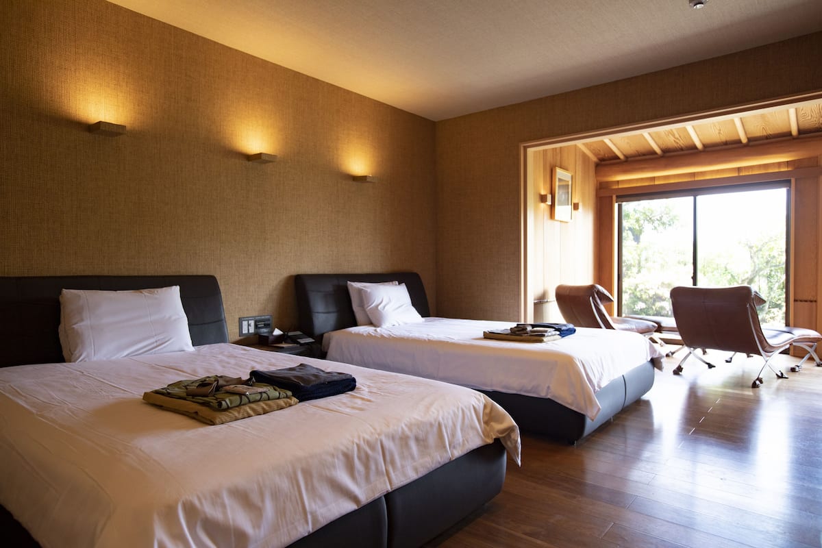 A hotel room with two beds, a desk, a chair, and a large window.