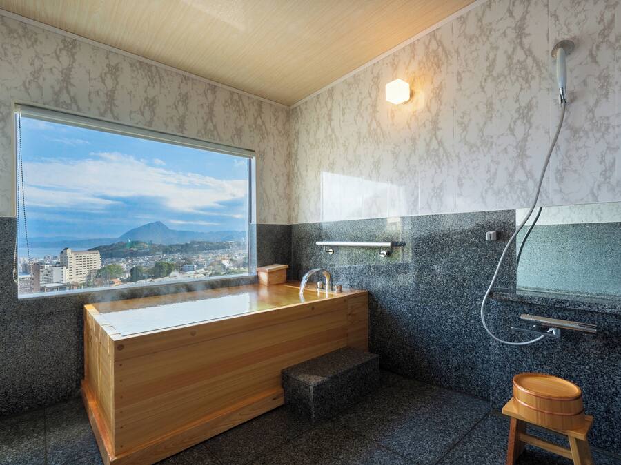 Un baño moderno con una bañera de madera, una ducha y vistas a un paisaje urbano a través de un ventanal grande.