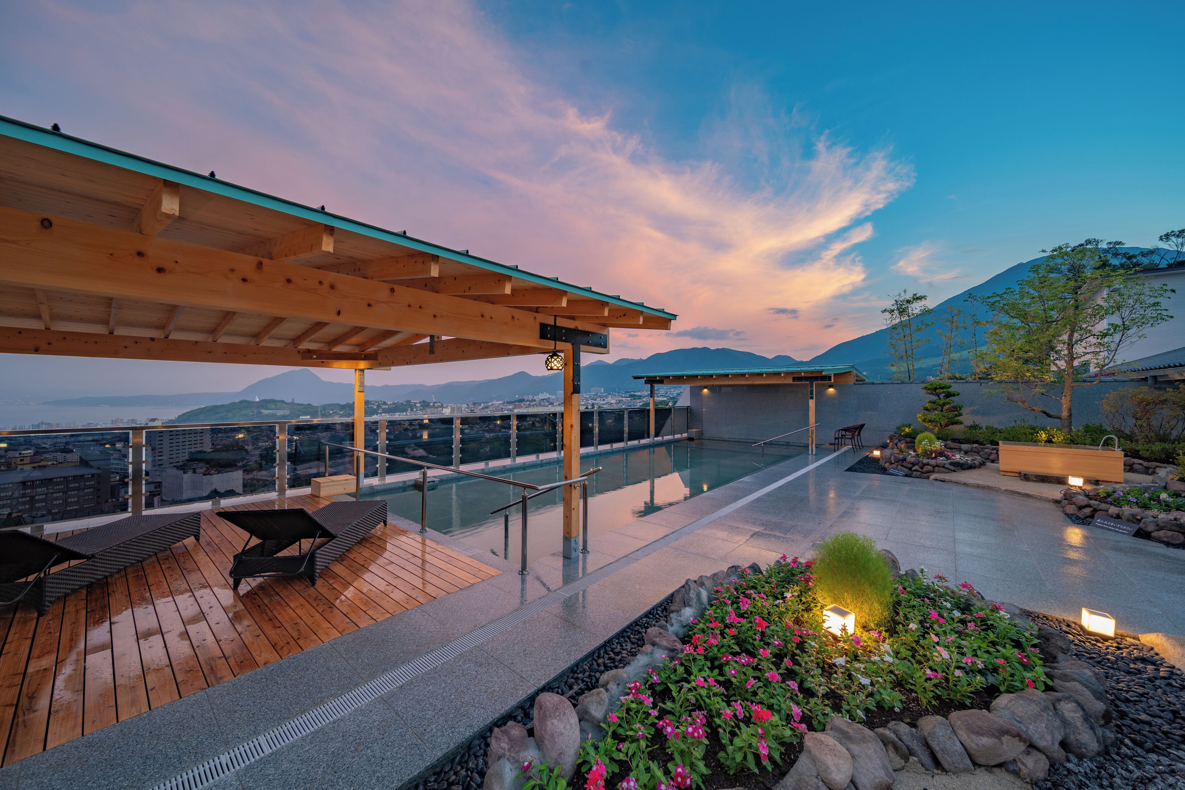 A rooftop terrace with a pool, seating area, and a view of the city and mountains.