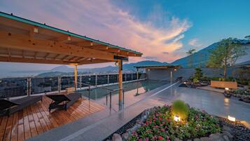 A rooftop terrace with a pool, seating area, and a view of the city and mountains.
