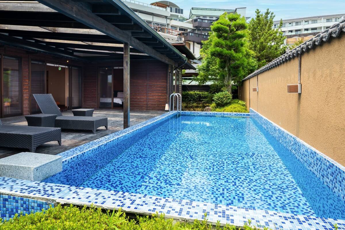 A swimming pool with blue mosaic tiles, surrounded by lounge chairs and a covered patio area.