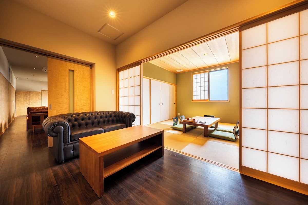 A traditional Japanese room with tatami flooring, a low wooden table, a black leather sofa, and sliding shoji screens.