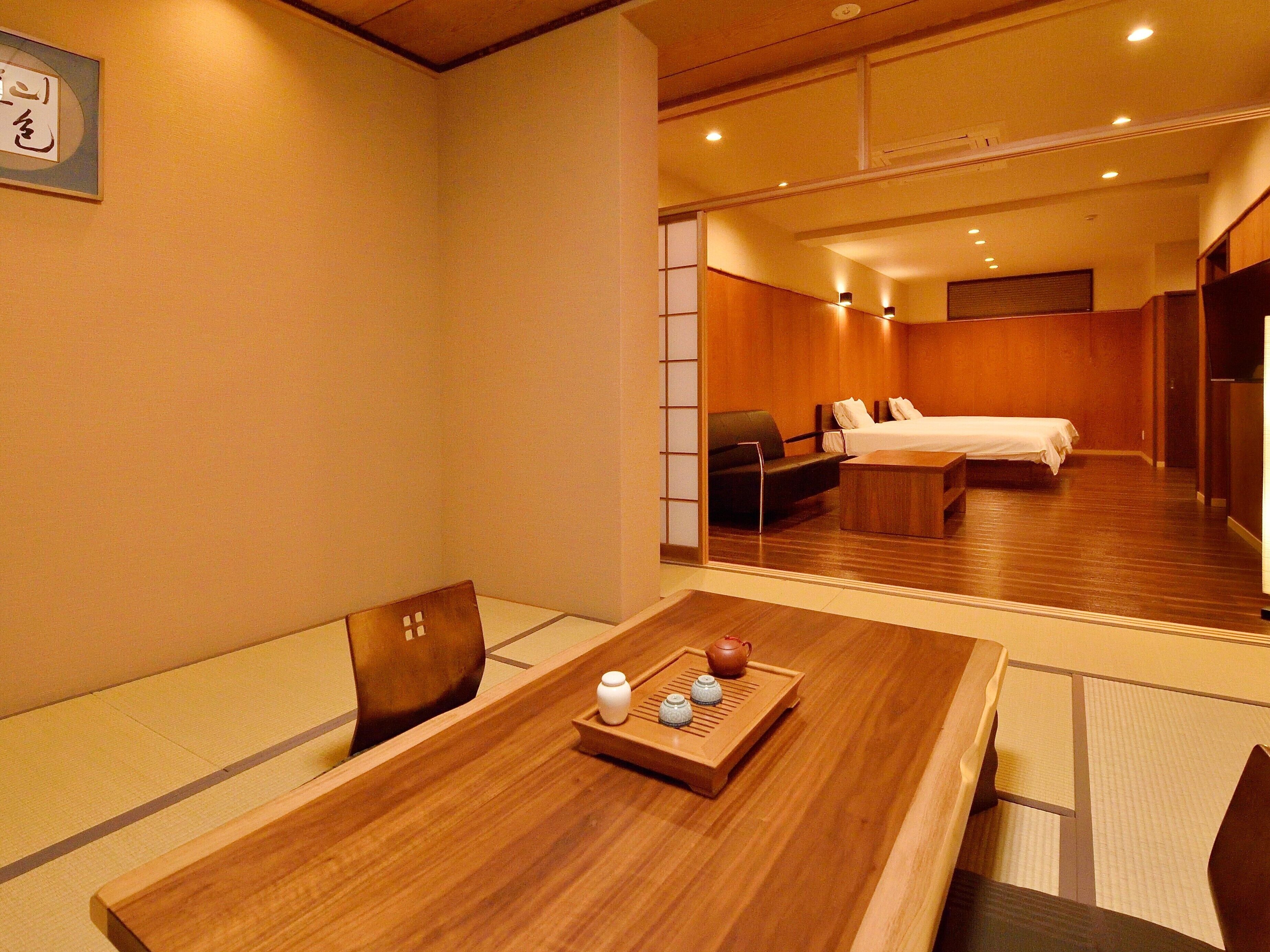 Habitación de hotel con una mesa de comedor de madera, una cama, un sofá y una pequeña mesa con tetera y tazas.