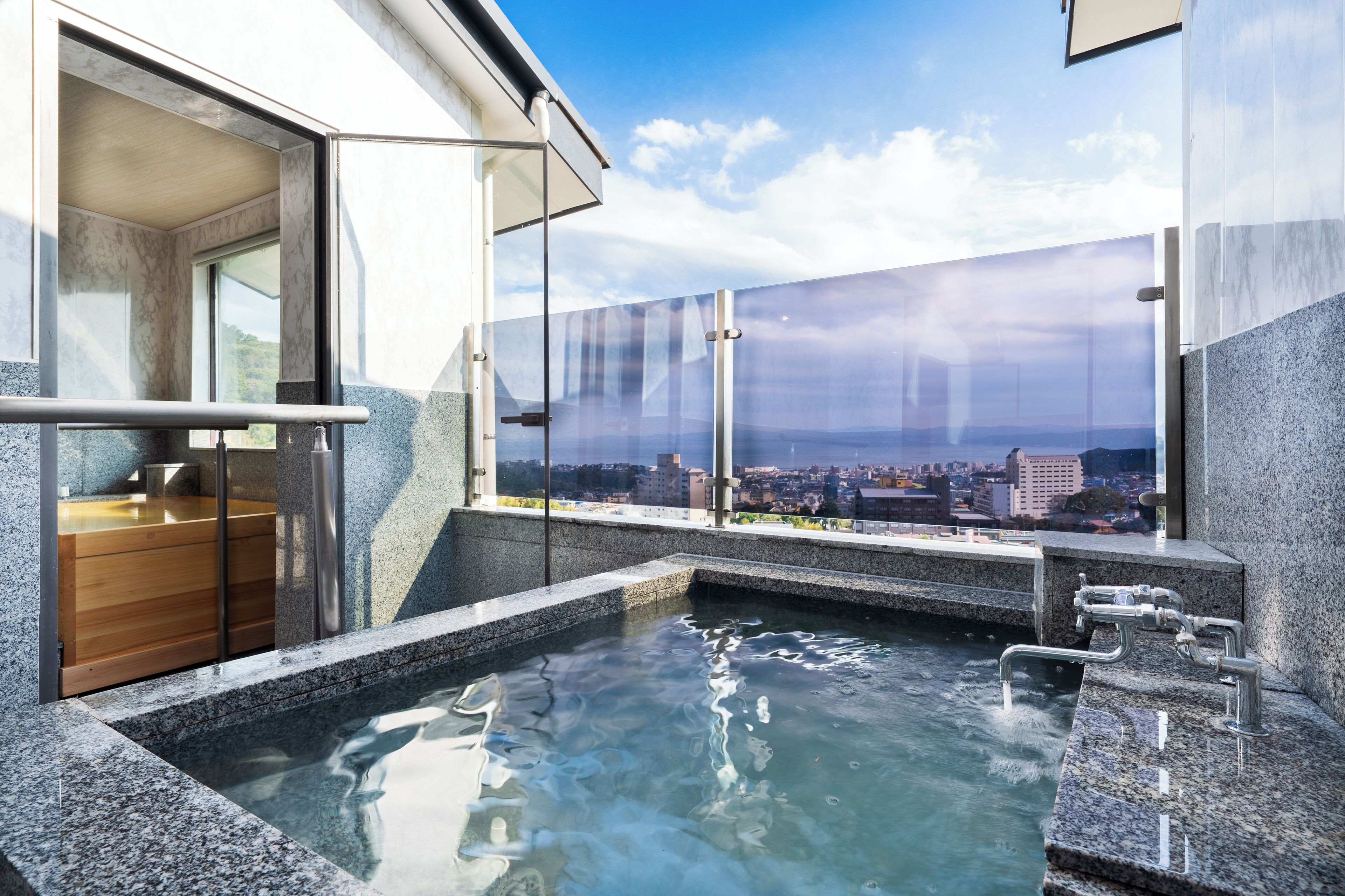 A modern spa area with a hot tub, wooden bath, and a city view through large glass windows.