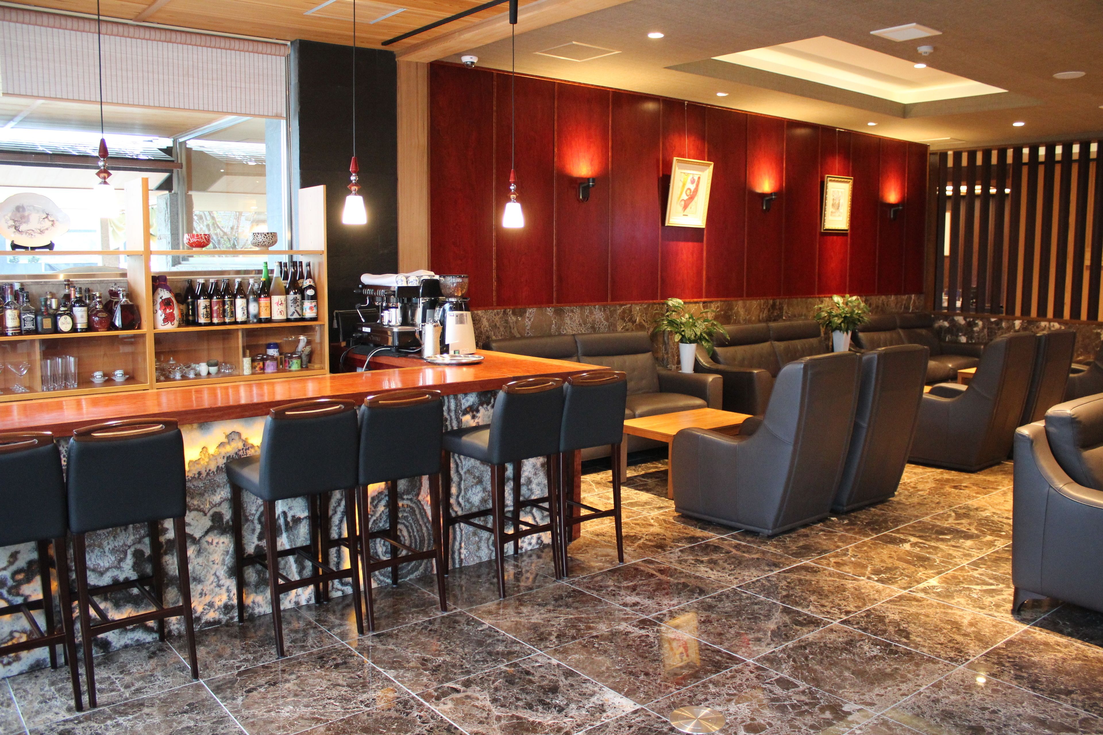 A bar area with a marble floor, bar stools, and a coffee machine. There are cushioned seating areas with armchairs and a sofa.