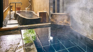 A hot spring bath area with a stone floor, a wooden bench, and a small wooden box.