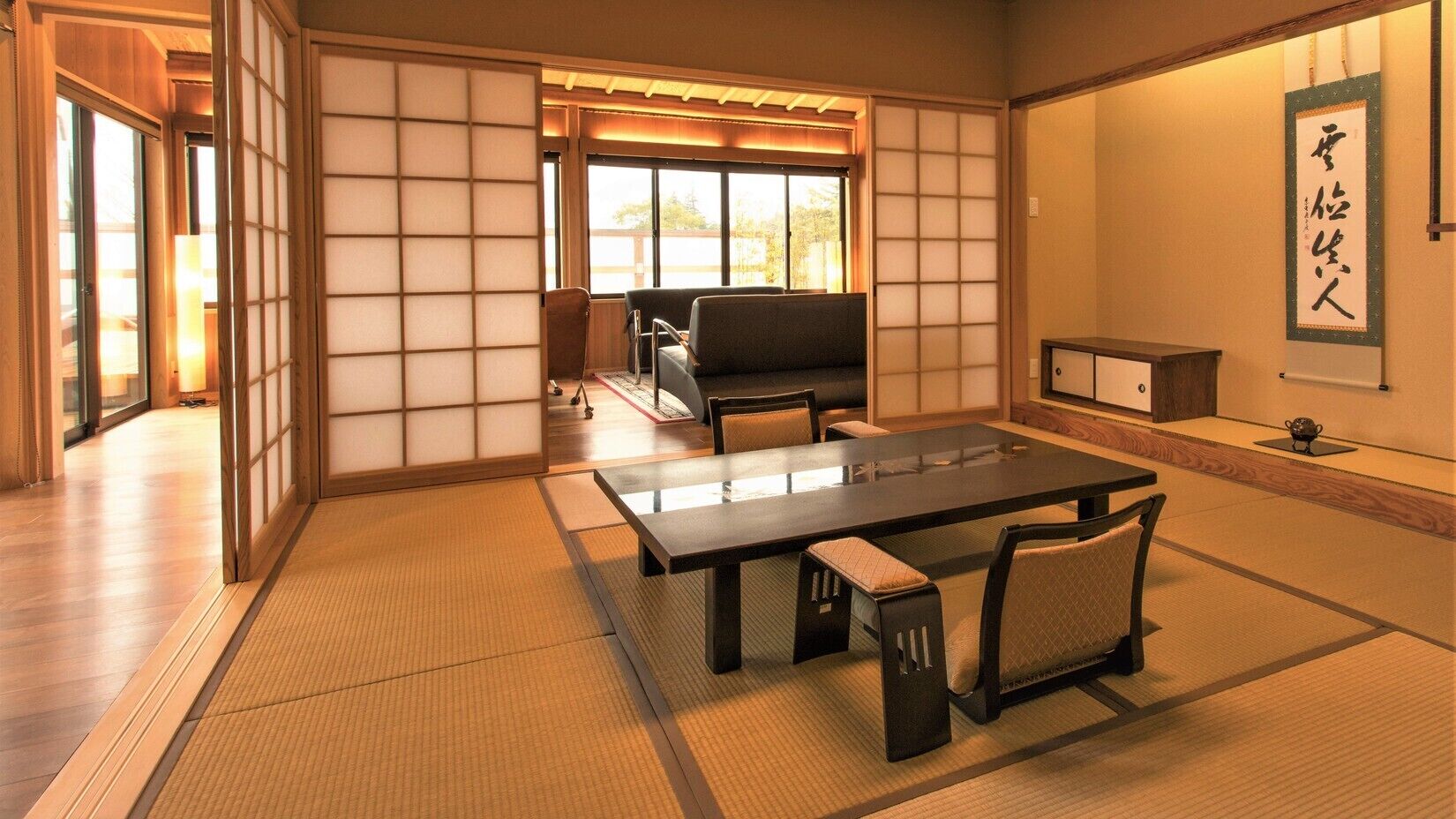 A tatami mat room with a low table and chairs, sliding doors, and a view through a window.